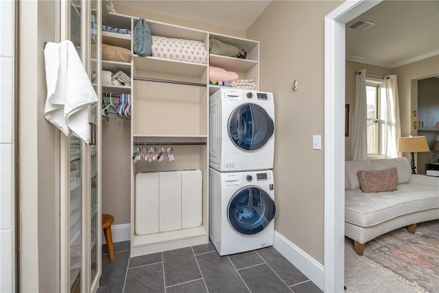 washroom with dark tile patterned flooring, crown molding, and stacked washer and clothes dryer