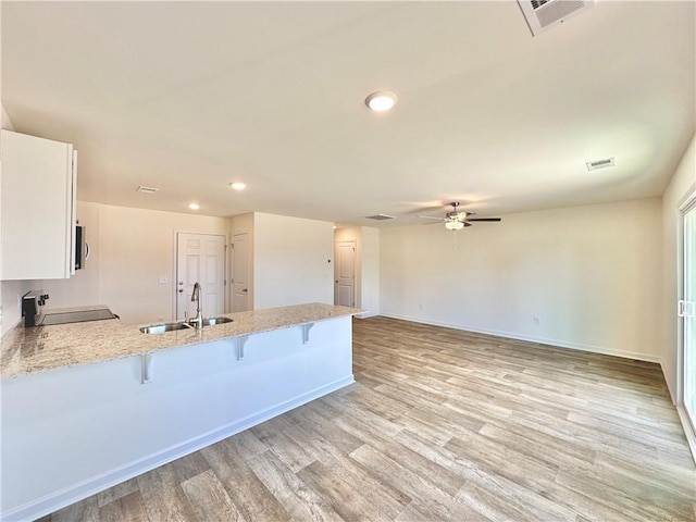 kitchen featuring a kitchen bar, sink, white cabinetry, kitchen peninsula, and light stone countertops