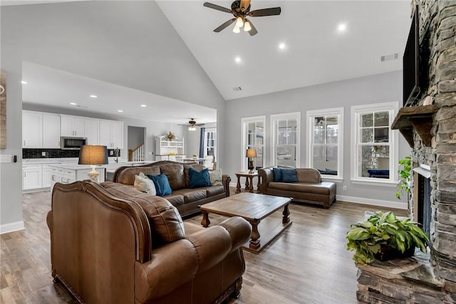 living room featuring ceiling fan, a stone fireplace, high vaulted ceiling, and light hardwood / wood-style flooring