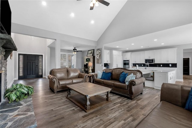 living room with a stone fireplace, ceiling fan, high vaulted ceiling, and wood-type flooring