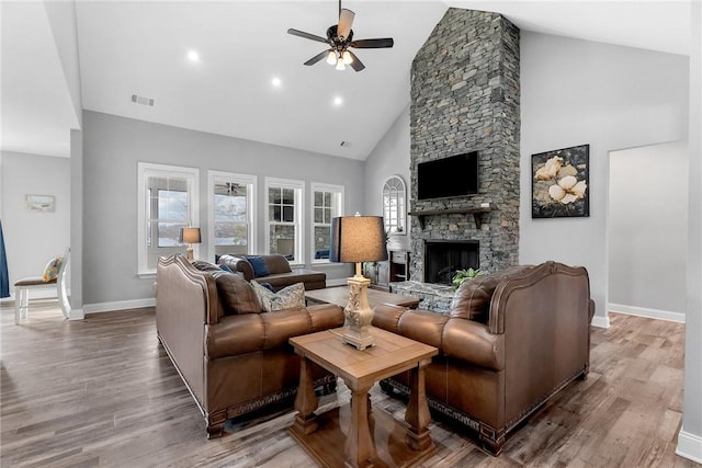 living room with wood-type flooring, high vaulted ceiling, a stone fireplace, and ceiling fan