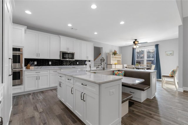 kitchen featuring a center island with sink, white cabinetry, dark wood-type flooring, and appliances with stainless steel finishes