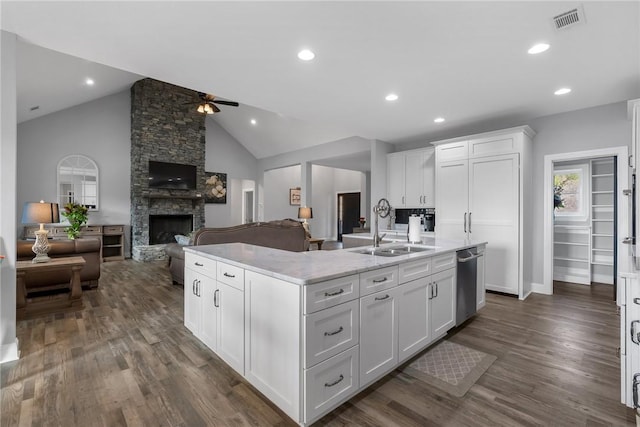 kitchen featuring a stone fireplace, white cabinetry, sink, and an island with sink