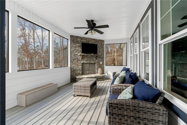 sunroom / solarium featuring ceiling fan and a stone fireplace