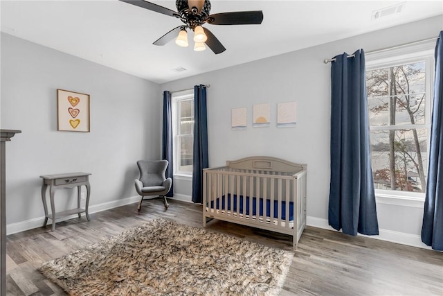 bedroom with a nursery area, hardwood / wood-style flooring, and ceiling fan