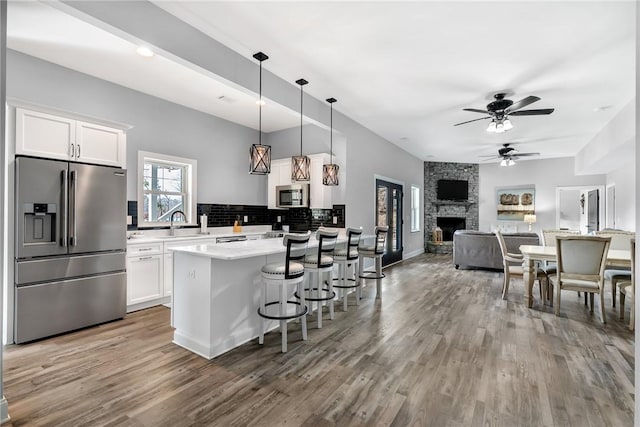 kitchen featuring decorative light fixtures, a stone fireplace, white cabinetry, and appliances with stainless steel finishes