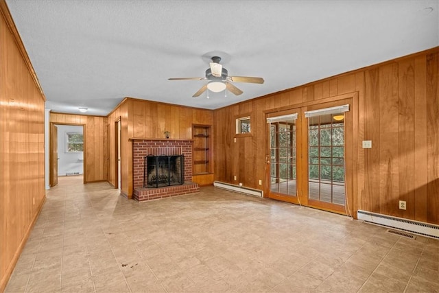 unfurnished living room with baseboard heating, ceiling fan, a fireplace, and wood walls