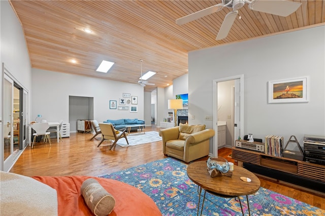 living room featuring a skylight, ceiling fan, light hardwood / wood-style flooring, a fireplace, and wood ceiling