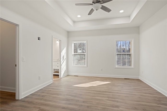 interior space with a raised ceiling, ceiling fan, and light wood-type flooring