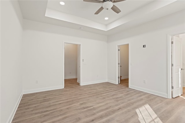 unfurnished room with a tray ceiling, ceiling fan, and light wood-type flooring