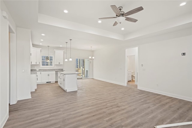 unfurnished living room with ceiling fan with notable chandelier, a tray ceiling, and light hardwood / wood-style flooring