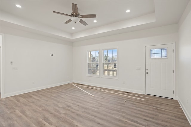 empty room with ceiling fan, a healthy amount of sunlight, a raised ceiling, and light wood-type flooring