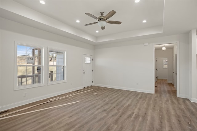 unfurnished living room featuring a tray ceiling, ceiling fan, and light wood-type flooring