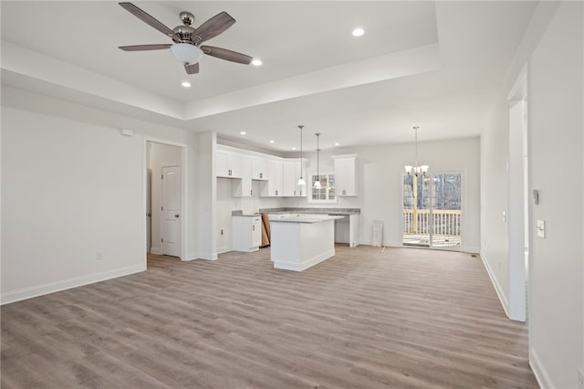 unfurnished living room featuring ceiling fan with notable chandelier, light wood-type flooring, and a tray ceiling