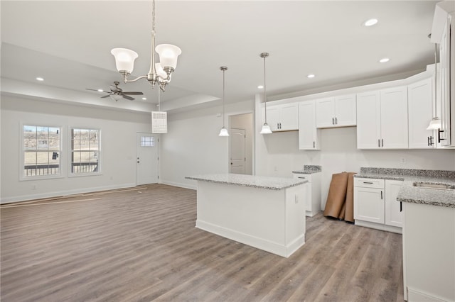 kitchen featuring white cabinets, ceiling fan with notable chandelier, light hardwood / wood-style flooring, decorative light fixtures, and a kitchen island