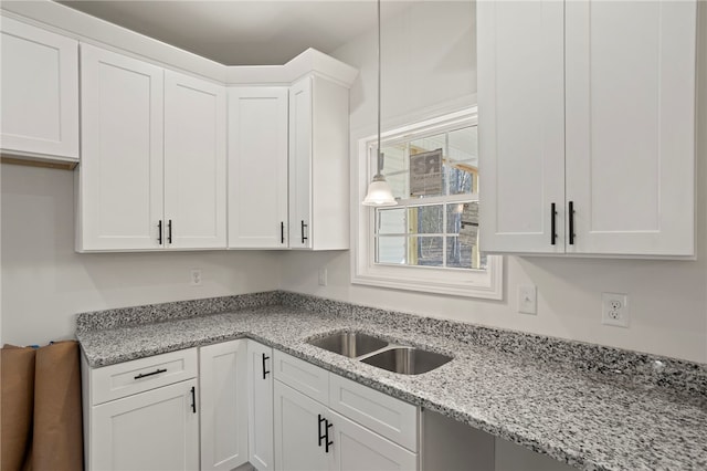 kitchen with white cabinets, decorative light fixtures, light stone countertops, and sink