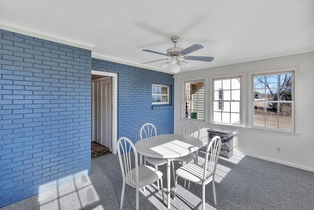 dining space featuring ceiling fan, dark carpet, crown molding, and brick wall