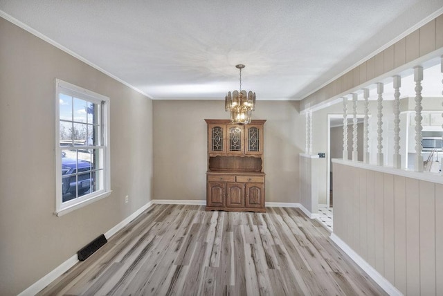 unfurnished dining area featuring a textured ceiling, light wood-type flooring, crown molding, and a chandelier