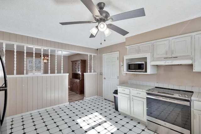 kitchen featuring white cabinets, appliances with stainless steel finishes, ceiling fan with notable chandelier, and wooden walls