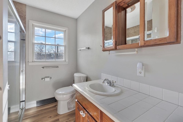 bathroom featuring wood-type flooring, a textured ceiling, toilet, a shower with door, and vanity