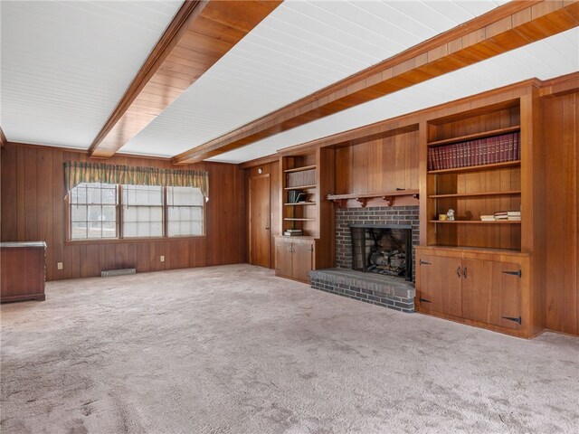 unfurnished living room with wooden walls, beamed ceiling, light colored carpet, and a brick fireplace