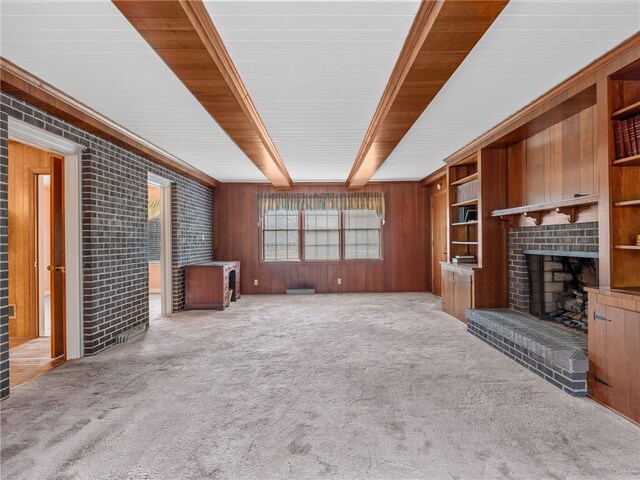 unfurnished living room featuring beam ceiling, wood walls, light carpet, and a brick fireplace