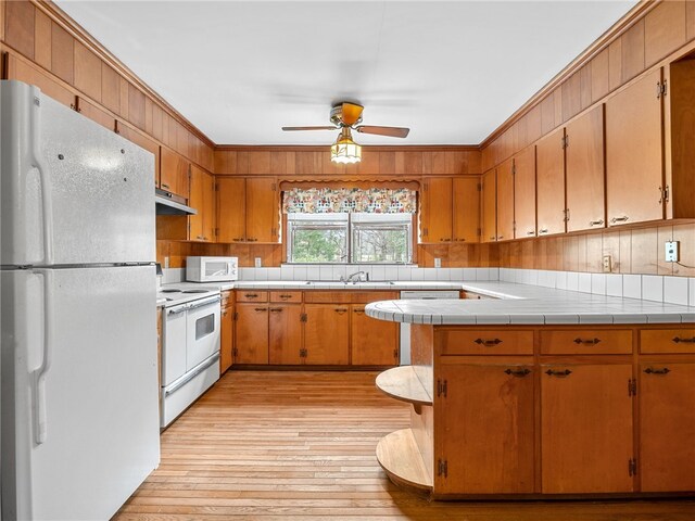 kitchen featuring light wood-type flooring, white appliances, ceiling fan, sink, and tile counters