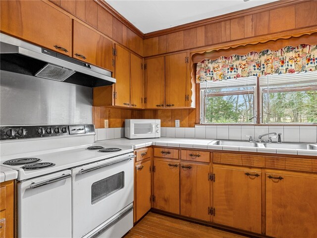 kitchen featuring white appliances, light hardwood / wood-style floors, tile counters, and sink