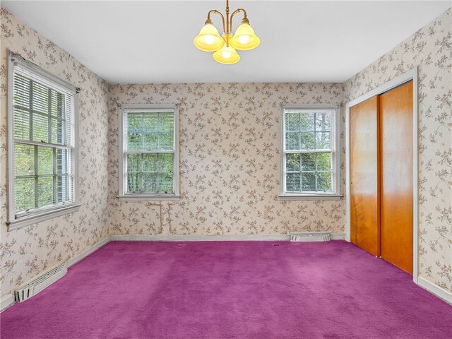 empty room featuring carpet, baseboard heating, a wealth of natural light, and an inviting chandelier