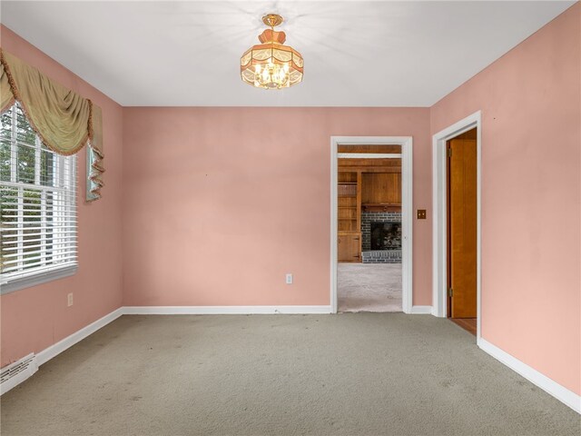 unfurnished room with carpet flooring, a chandelier, a healthy amount of sunlight, and a brick fireplace