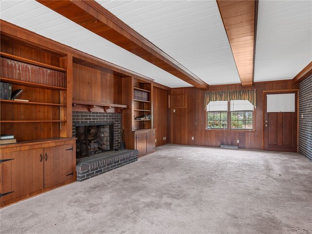 unfurnished living room with beam ceiling, wood walls, light carpet, and a brick fireplace