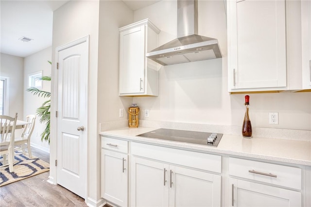 kitchen featuring black electric cooktop, wall chimney exhaust hood, light hardwood / wood-style floors, and white cabinets