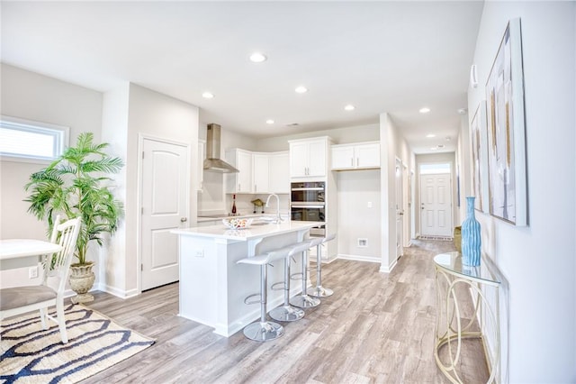 kitchen with sink, white cabinets, a kitchen breakfast bar, a kitchen island with sink, and wall chimney exhaust hood