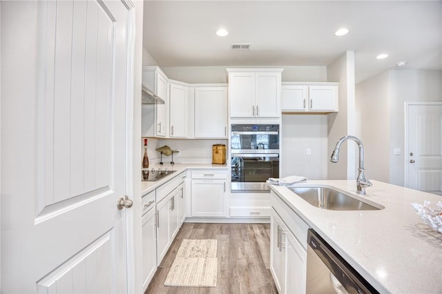 kitchen with sink, light stone counters, light wood-type flooring, appliances with stainless steel finishes, and white cabinets