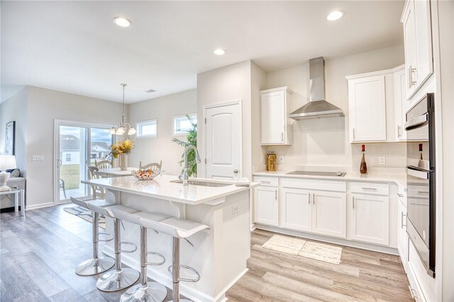 kitchen featuring pendant lighting, sink, white cabinets, black electric cooktop, and wall chimney exhaust hood