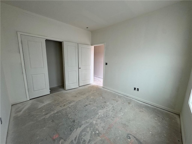 unfurnished bedroom featuring concrete flooring, a closet, and baseboards