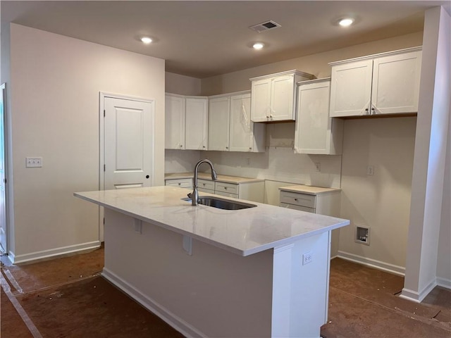 kitchen with visible vents, baseboards, light stone countertops, a center island with sink, and a sink