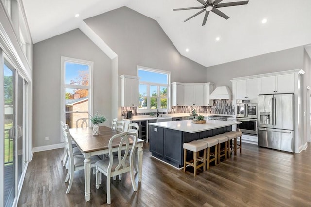 kitchen featuring white cabinetry, a center island, stainless steel appliances, high vaulted ceiling, and decorative backsplash