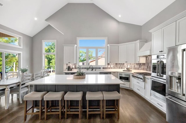 kitchen with stainless steel appliances, a kitchen island, high vaulted ceiling, backsplash, and white cabinets