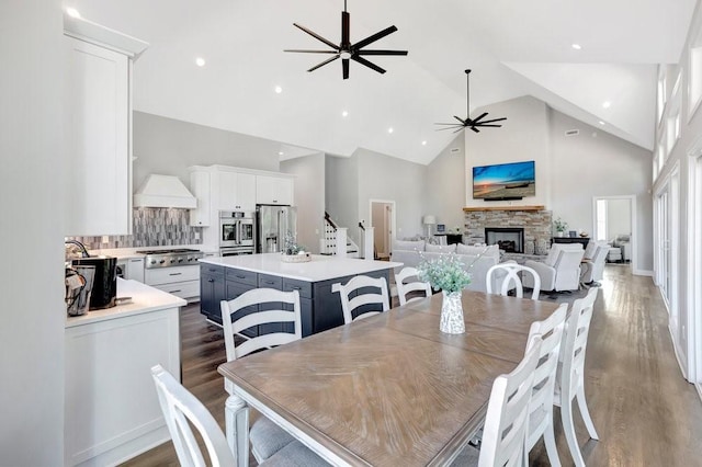 dining space with dark hardwood / wood-style floors, ceiling fan, a stone fireplace, and high vaulted ceiling