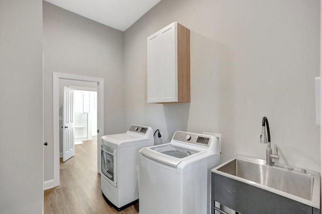 laundry area featuring cabinets, light hardwood / wood-style floors, washing machine and clothes dryer, and sink