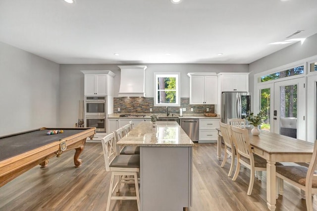 kitchen featuring a center island, pool table, light stone counters, custom range hood, and stainless steel appliances