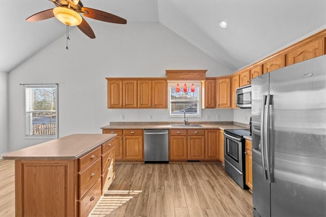 kitchen with ceiling fan, sink, stainless steel appliances, a kitchen island, and light wood-type flooring