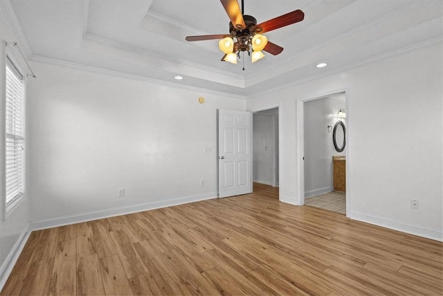 unfurnished bedroom with ceiling fan, ensuite bathroom, crown molding, a tray ceiling, and light wood-type flooring