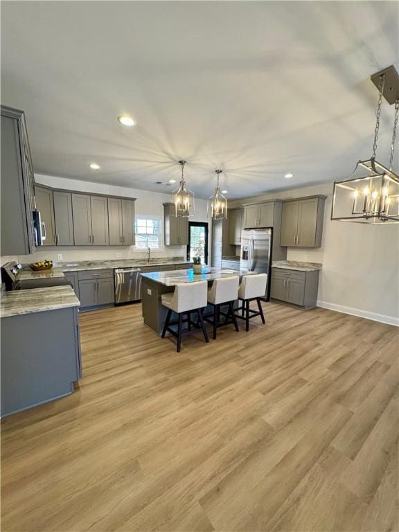 kitchen with light stone countertops, a center island, stainless steel appliances, light hardwood / wood-style flooring, and decorative light fixtures