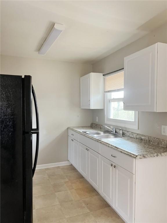 kitchen with black refrigerator, white cabinetry, and sink