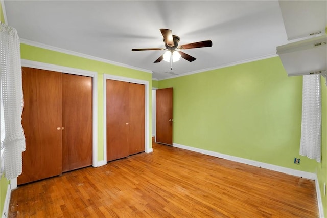 unfurnished bedroom featuring ceiling fan, light hardwood / wood-style floors, ornamental molding, and two closets