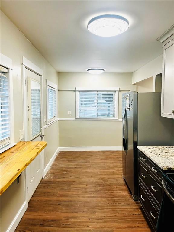 kitchen with stainless steel fridge, light stone countertops, white cabinets, and dark wood-type flooring