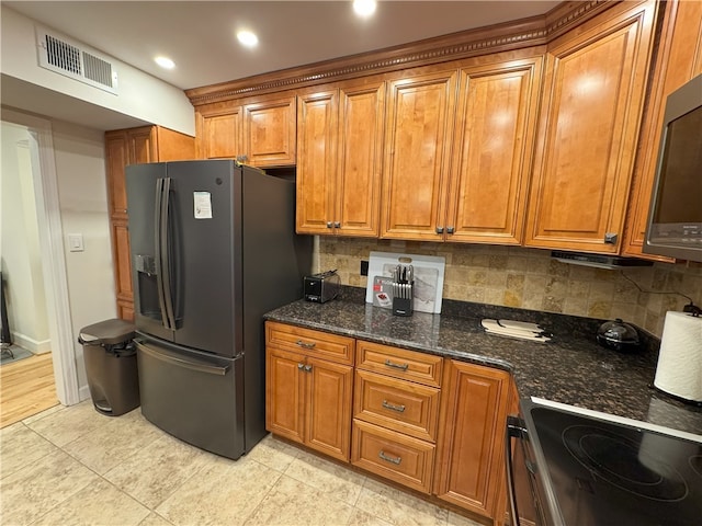 kitchen featuring decorative backsplash, dark stone counters, light tile patterned floors, black electric range, and stainless steel fridge with ice dispenser