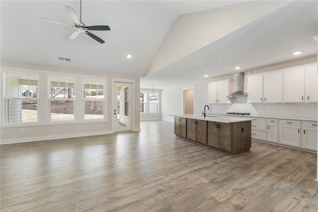 kitchen with white cabinetry, a center island with sink, wall chimney exhaust hood, and ceiling fan